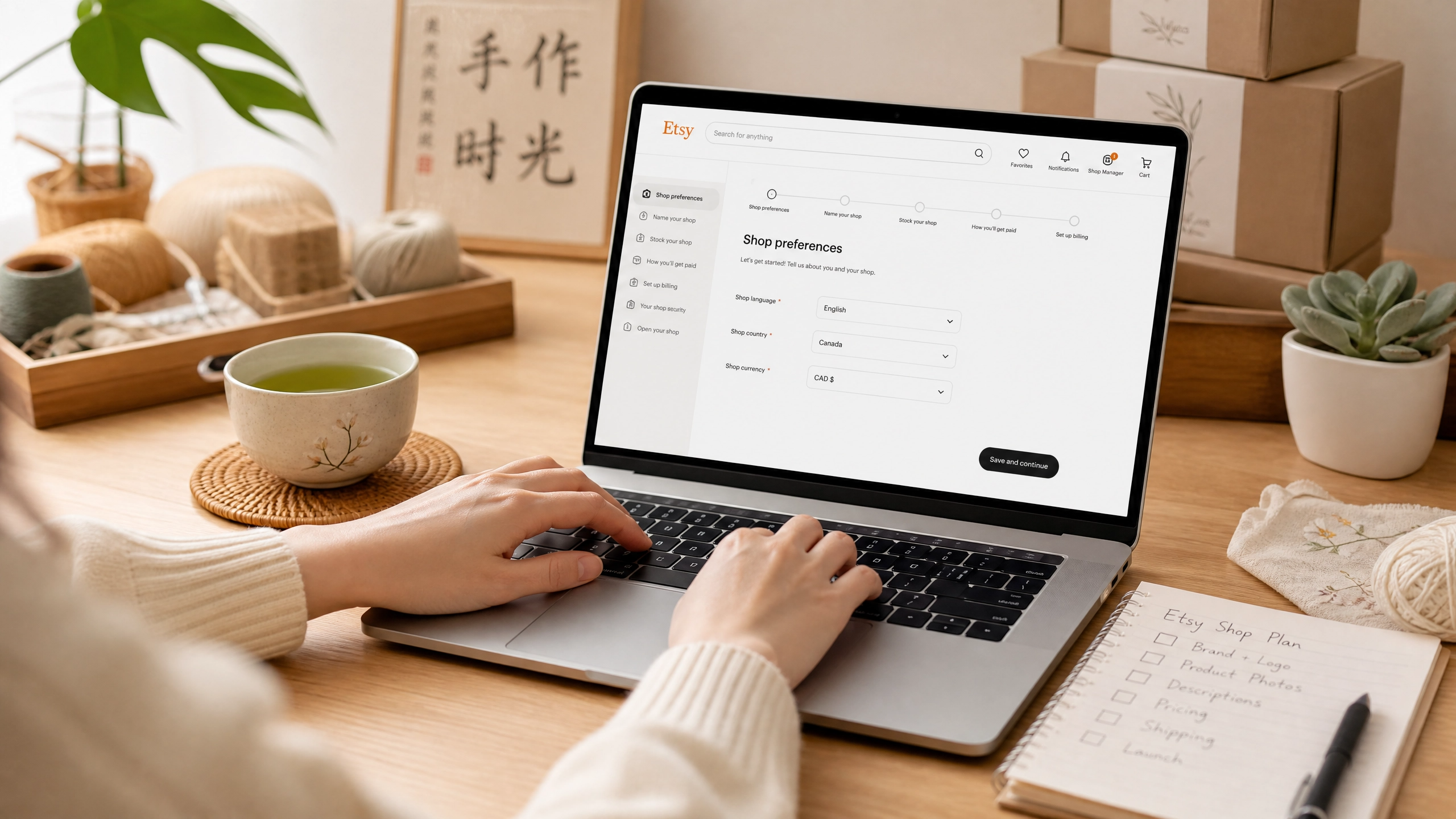 Asian entrepreneur typing on a MacBook, setting up an Etsy shop with craft supplies nearby.